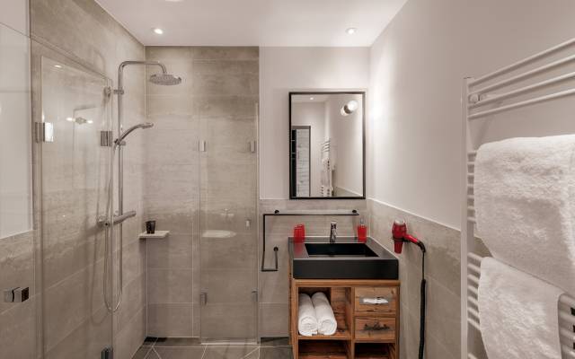 Ein helles Badezimmer im Hotel Traumschmiede: ausgestattet mit Natursteinfliesen, einem hölzernen Waschtisch und einer Handtuchheizung