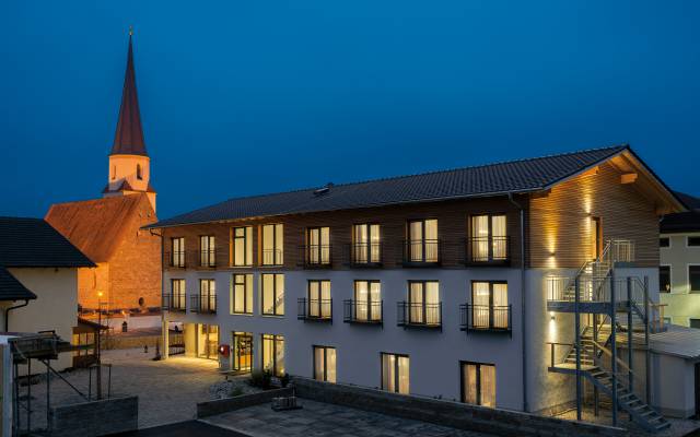 Eine Außenansicht des Hotels Traumschmiede bei Nacht - im Hintergrund ist die Kirche von Unterneukirchen sichtbar
