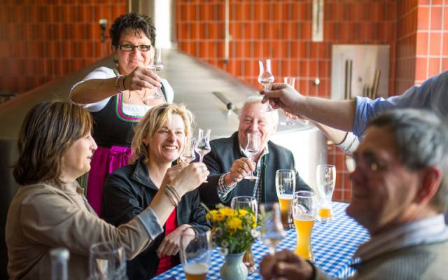 Die Hotelgäste der Traumschmiede stoßen lachend während ihrer Bier-Wanderung in einer Brauerei an 